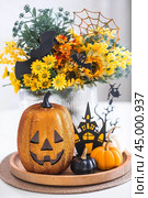 A vase of flowers, pumpkins and a scary castle with a witch on the background of a Scandi-style white kitchen interior. The concept of home and comfort. Autumn decor for Halloween. Стоковое фото, фотограф Photojuli / Фотобанк Лори