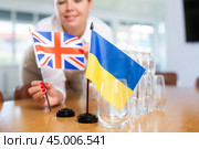 Unrecognizable girl sets midget Ukrainian and Britannic flags before international negotiations. Стоковое фото, фотограф Яков Филимонов / Фотобанк Лори