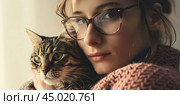 Young beautiful smiling brunette woman holds your tabby cat in her hands isolated on a light gray background. Good friends. Friendship of a pet and its owner girl. Cuddles. Copy space for text banner. Стоковое AI-изображение, AI-художник Марина Демидюк / Фотобанк Лори