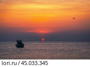 The plane is landing flying over a fishing boat bobbing on the waves against the background of a beautiful sunset. Стоковое фото, фотограф Игорь Кляхин / Фотобанк Лори