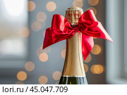 Champagne bottle with a red bow tie celebrating christmas or new year eve. Стоковое AI-изображение, AI-художник Иван Рябоконь / Фотобанк Лори