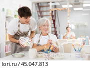 Guy assisting senior woman painting ceramic mug in pottery class. Стоковое фото, фотограф Яков Филимонов / Фотобанк Лори