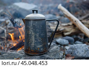 Old sooty coffee pot warming on rocks by campfire. Стоковое AI-изображение, AI-художник Иван Рябоконь / Фотобанк Лори