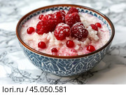 Bowl of rice pudding with fresh raspberries and redcurrants being sprinkled with powdered sugar. Стоковое AI-изображение, AI-художник Иван Рябоконь / Фотобанк Лори