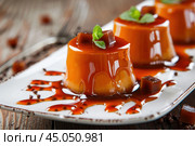 Creamy caramel puddings topped with sauce and mint on white plate. Стоковое AI-изображение, AI-художник Иван Рябоконь / Фотобанк Лори