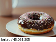 Delicious chocolate donut covered with sprinkles resting on white plate. Стоковое AI-изображение, AI-художник Иван Рябоконь / Фотобанк Лори