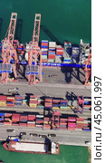Cranes loading and unloading cargo create a lively scene at a bustling port, highlighting dockworkers as they maneuver containers under bright, sunny skies. Стоковое видео, видеограф ILIA GOROKHOV / Фотобанк Лори
