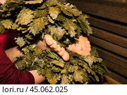 Russian bath house, woman in red bathrobe whip with brooms steamed man foot, with hot steam, close-up. Male lying down relaxing on wood bench. Wellness, self-care, healthy concept. Copy ad text space. Стоковое фото, фотограф Aleksandr Golubev / Фотобанк Лори
