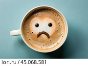 A mug of coffee with a sad smiley face on the foam on the blue table. Top view, flat lay. Стоковое AI-изображение, AI-художник Photojuli / Фотобанк Лори