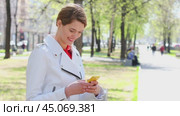 SMS. Young beautiful girl reads messages on cellphone sitting on bench in park. Стоковое видео, видеограф Андрей Аркуша / Фотобанк Лори