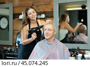 Girl hairdresser completes creation of haircut and dries hair with hairdryer to elderly male client. Стоковое фото, фотограф Яков Филимонов / Фотобанк Лори