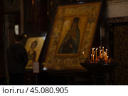 Candles burn in a candlestick in a semi-dark room of an Orthodox church against the backdrop of icons (2024 год). Редакционное фото, фотограф Евгений Харитонов / Фотобанк Лори