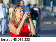 Moscow, Russia, August 2018: Senior woman takes a pictures on the phone on a background of a  crowd of tourists on the Red Square (editorial) Редакционное фото, фотограф Михаил Строгалев / Фотобанк Лори