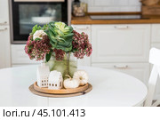 Still-life. A bouquet of decorative cabbage in a vase, pumpkins and white houses on the table in the interior of a home kitchen. A cozy autumn concept. Стоковое фото, фотограф Photojuli / Фотобанк Лори