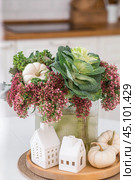 Still-life. A bouquet of decorative cabbage in a vase, pumpkins and white houses on the table in the interior of a home kitchen. A cozy autumn concept. Стоковое фото, фотограф Photojuli / Фотобанк Лори