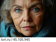 Close-up of an elderly woman's face with grey hair and expressive blue eyes. Her face shows wrinkles and traces of years lived, which symbolizes wisdom and experience. The woman is wrapped in a warm blue scarf, which creates a feeling of coziness and warmth. The photograph conveys emotional depth, calmness and dignity. Стоковое AI-изображение, AI-художник Анна Кривицкая / Фотобанк Лори