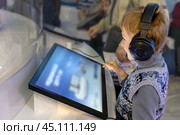 Boy wearing headphones interacts with interactive screen at an exhibit. Стоковое фото, фотограф Алла Чесноковва / Фотобанк Лори