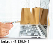 woman sitting at table, looking at laptop, pay for purchases by credit card, online shopping. Стоковое фото, фотограф Natalia Gdovskaia / Фотобанк Лори