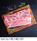 Big whole piece of pork meat with seasoning on chopping board on dark. Стоковое фото, фотограф Natalia Gdovskaia / Фотобанк Лори