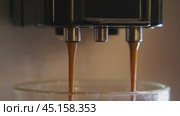 A close-up of an espresso machine making coffee. Two streams of dark brown espresso drip into a glass cup and then pour out in a stream. Стоковое видео, видеограф Воловодов Владимир / Фотобанк Лори