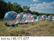 Many zorb balls laying in grass field under summer sun. Стоковое AI-изображение, AI-художник Иван Рябоконь / Фотобанк Лори
