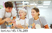 cheerful elderly woman, along with a young girl and a guy in aprons, are engaged in painting ceramic dishes at a pottery lesson. Стоковое видео, видеограф Яков Филимонов / Фотобанк Лори