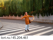 Middle aged woman dancing standing on a crosswalk. Full length portrait of a mature woman happily twirling on the road 50 year old woman (fifty years old) Стоковое фото, фотограф Андрей Журавлев / Фотобанк Лори