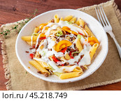 Penne pasta with yellow tomatoes, vegetables, mincemeat, white sauce on dark wooden background, side view, close up. Стоковое фото, фотограф Natalia Gdovskaia / Фотобанк Лори