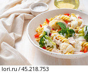 Pasta fusilli with vegetables, boiled steamed meat, white sauce on white wooden table. Стоковое фото, фотограф Natalia Gdovskaia / Фотобанк Лори