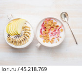 Two greek yogurt with jam, apple, muesli, chia seeds and banana in white bowl on white wooden table, top view. Стоковое фото, фотограф Natalia Gdovskaia / Фотобанк Лори