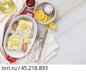 cod fish fillet, freshly cooked in oven with onion in red porcelain dish for baking. Стоковое фото, фотограф Natalia Gdovskaia / Фотобанк Лори
