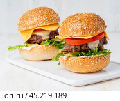 Two hamburgers on white board on white background, hot homemade unhealthy fat food. Стоковое фото, фотограф Natalia Gdovskaia / Фотобанк Лори