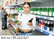 Young female shopper choosing Korean soju bottle at liquor store. Стоковое фото, фотограф Яков Филимонов / Фотобанк Лори