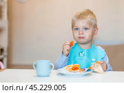 Unhealthy food for children. Eating. A cute 2-year-old kid eats pizza for lunch. Fast food. Family and children. Стоковое фото, фотограф Photojuli / Фотобанк Лори