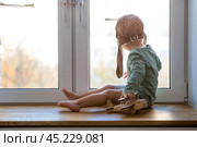 A cute 2-year-old boy in a cap is playing on the windowsill with a wooden airplane. Children's wooden toys for child development. Стоковое фото, фотограф Photojuli / Фотобанк Лори