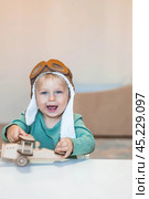 A handsome little boy of 2 years old in a pilot's hat is playing with a wooden airplane and a logistics constructor. Children's wooden toys for child development. Стоковое фото, фотограф Photojuli / Фотобанк Лори