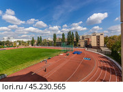 Znamensky Brothers stadium, Stromynka 4 - 03.09.2019: An aerial view of a red running track and soccer field, surrounded by a fence and green trees. The school's buildings are in the background, along with a blue sky and puffy white clouds. Стоковое фото, фотограф Алексей Климкин / Фотобанк Лори