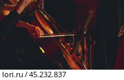 A man playing the cello. The musician's hands are clearly visible, one holding the bow and the other resting on the cello's fingerboard. The violinist is blurred in the foreground. Close-up. Стоковое видео, видеограф Воловодов Владимир / Фотобанк Лори