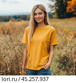 Young woman standing against the backdrop of an autumn field. She is wearing a bright yellow t-shirt and blue jeans, which contrasts beautifully with the natural surroundings. A slight smile and calm expression create an atmosphere of warmth and comfort. The autumn background with golden and brown tones emphasizes the naturalness and beauty of the surrounding nature, and also harmonizes with the model's clothes. Стоковое AI-изображение, AI-художник Анна Кривицкая / Фотобанк Лори