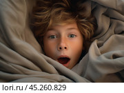 Top view, portrait of Boy with freckles lied in bed under blanket and yawns with wide opened mouth. He surprised, screaming or startled. Kid is surrounded by grey pillow and blanket. Стоковое AI-изображение, AI-художник Sergey Grishin / Фотобанк Лори