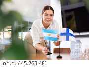 Positive young woman putting flag of Argentina on the table with flag of Finland in conference room. Стоковое фото, фотограф Яков Филимонов / Фотобанк Лори