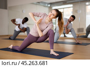 Woman doing Parivrtta Anjaneyasana in kneeling position in fitness studio. Стоковое фото, фотограф Яков Филимонов / Фотобанк Лори