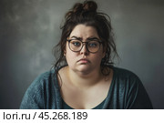 Ugly Young plus size woman wearing casual clothes and glasses sad expression on face with grey background. Apathy, depression, bulling, harassments concept. Social problem of fat people. Стоковое AI-изображение, AI-художник Sergey Grishin / Фотобанк Лори