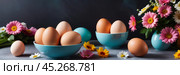 A bowl of colorful painted easter eggs on a table with first bright spring flowers. Concept of Pascha, Resurrection Sunday, Christian cultural holiday. Banner, copy space. Стоковое AI-изображение, AI-художник Sergey Grishin / Фотобанк Лори