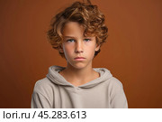 Portrait of disgruntled blond boy against brown background. The boy experiencing negative emotions due to fact that his family tore him away from computer games and forced him. Sulking Caucasian boy. Стоковое AI-изображение, AI-художник Sergey Grishin / Фотобанк Лори