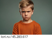 Portrait of disgruntled blond boy against grey background. The boy experiencing negative emotions due to fact that his family tore him away from computer games and forced him. Sulking Caucasian boy. Стоковое AI-изображение, AI-художник Sergey Grishin / Фотобанк Лори