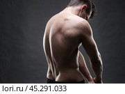 Handsome muscular bodybuilder posing on gray background. Low key studio shot. Стоковое фото, фотограф Станислав Тарко / Фотобанк Лори