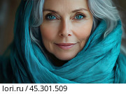 An older woman with grey hair and bright blue eyes, wrapped in a soft, turquoise scarf that frames her face. Her gaze is calm and confident, her facial expression is warm and wise, conveying inner peace and strength. The texture of her skin highlights the natural beauty of age, adding realism and warmth to the photo. The photo is highly detailed and softly lit, focusing on her eyes and facial features. Стоковое AI-изображение, AI-художник Анна Кривицкая / Фотобанк Лори