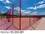 A vibrant red sports court surrounded by fencing in a sunny park setting on a clear day. Стоковое фото, фотограф Алексей Климкин / Фотобанк Лори
