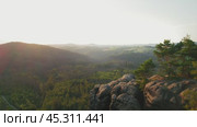 Hiker standing confidently on the rocky cliff edge, looking at the sprawling landscape in the early morning light. Стоковое видео, видеограф Ольга Сухарева / Фотобанк Лори